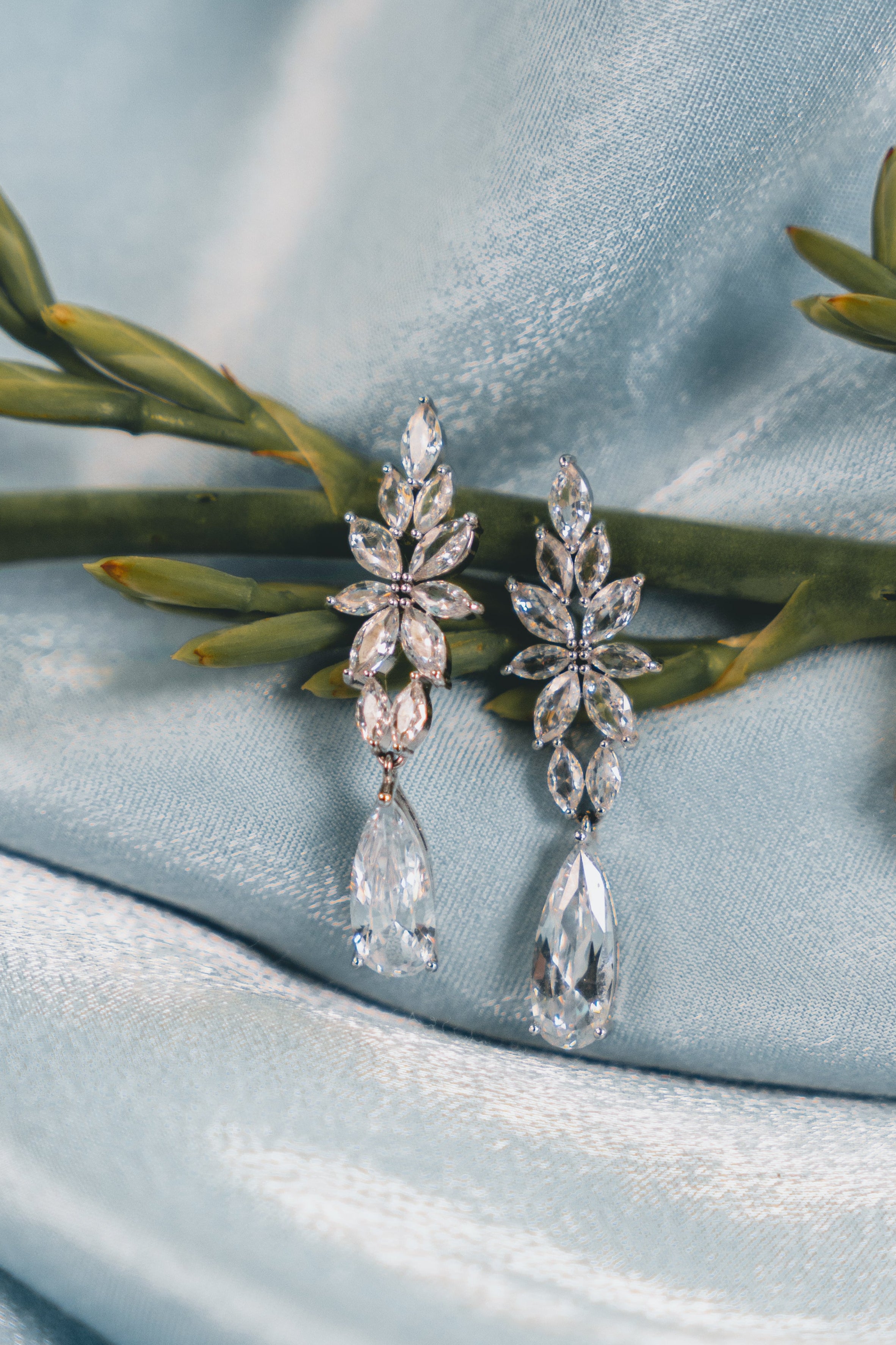 Pair of silver earrings on a light blue fabric background