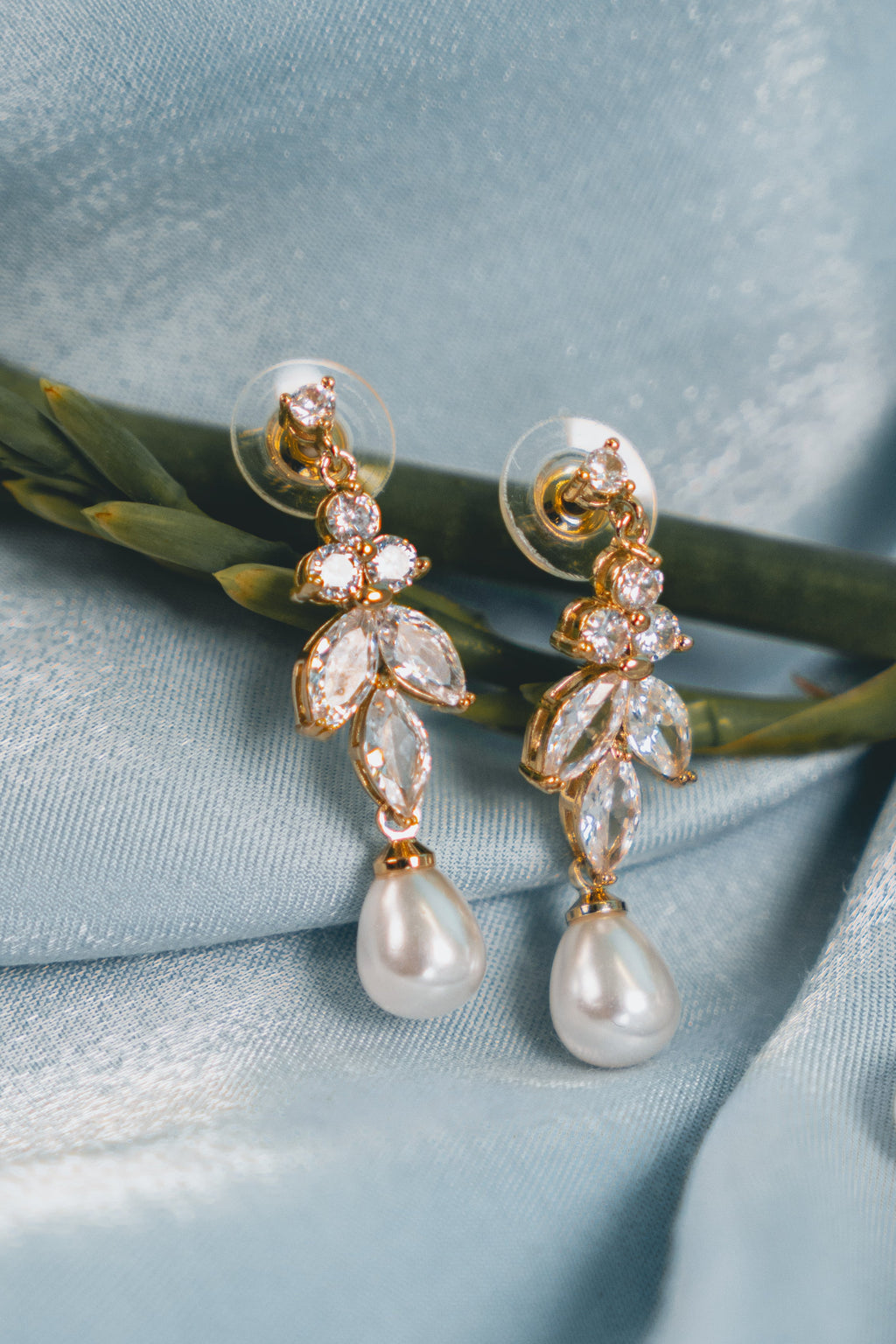 Pearl earrings with gold leaves on a light blue fabric background