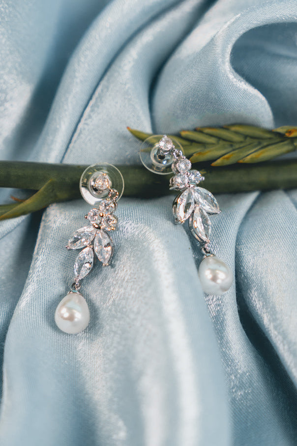 Pearl and crystal earrings on a light blue fabric background