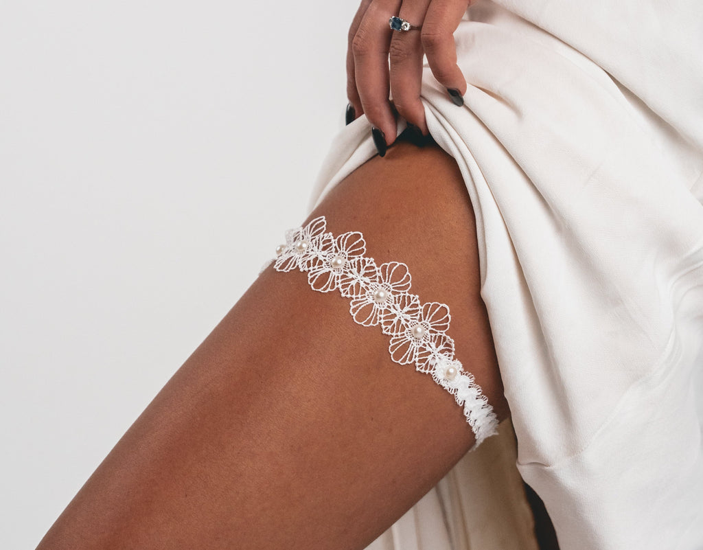 Close-up of a leg wearing a white lace garter with a neutral background